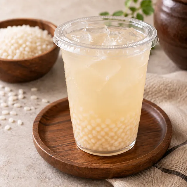 Iced sikhye in a clear cup, rice grains settled at the bottom, on a wooden plate